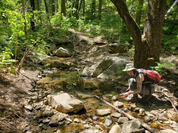 young woman crouched near a river collecting samples