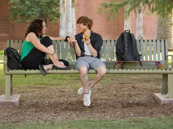 Two students sitting on a bench and talking on University of Arizona campus.