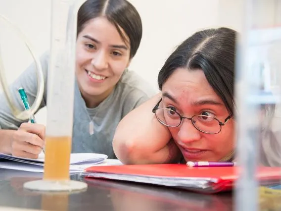 Two students observing a beaker with liquids in a lab.