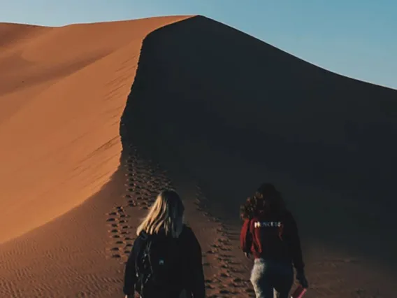 Two people walking over the crest of a sand dune.