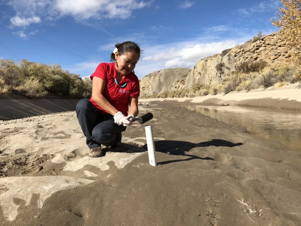 Karletta Chief collects a sediment core sample from a river to measure for contaminants.